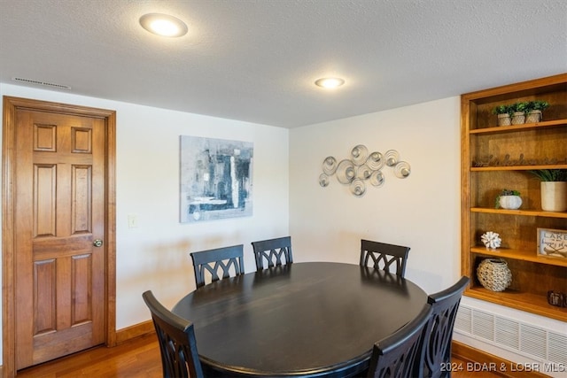 dining room with hardwood / wood-style flooring, a textured ceiling, and radiator heating unit