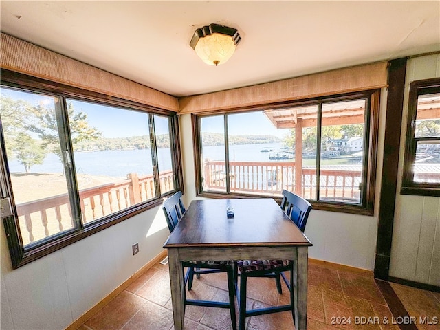 dining room featuring a water view, stone tile flooring, and baseboards