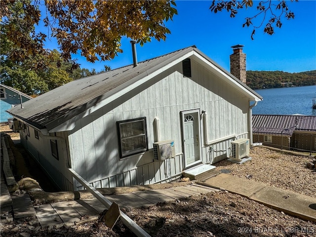 view of side of property with ac unit, a water view, and a chimney