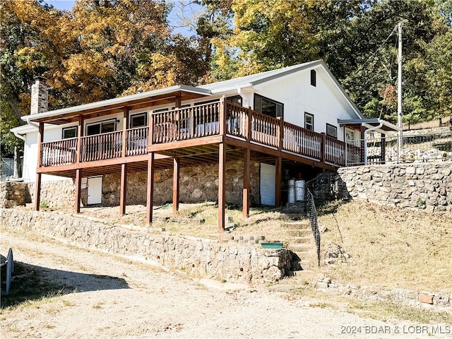 back of house with a chimney, stone siding, and a deck