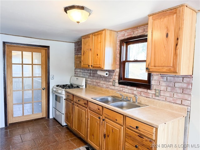 kitchen with decorative backsplash, stone finish floor, light countertops, white gas stove, and a sink