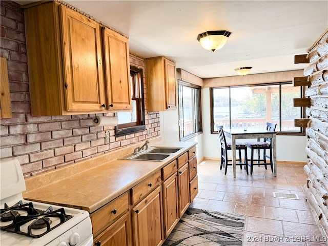 kitchen featuring stone tile floors, a sink, light countertops, brown cabinets, and white gas range