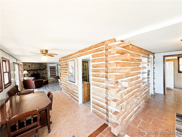 dining area with a fireplace, rustic walls, and a ceiling fan