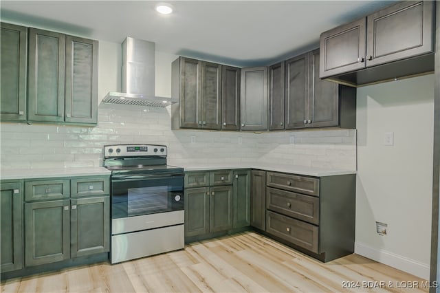 kitchen with electric stove, green cabinets, wall chimney exhaust hood, decorative backsplash, and light hardwood / wood-style flooring