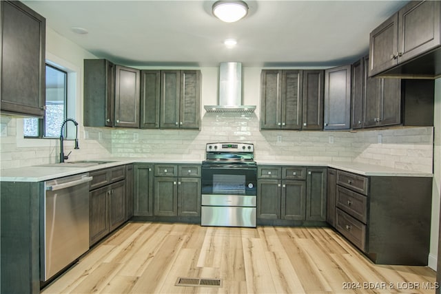 kitchen featuring appliances with stainless steel finishes, wall chimney exhaust hood, sink, and light wood-type flooring