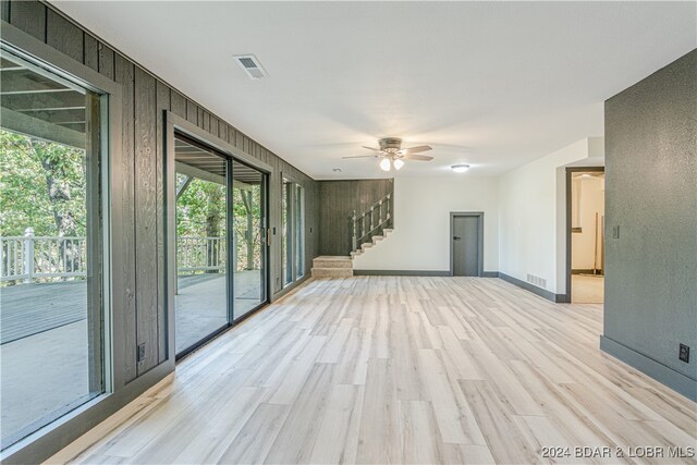 unfurnished living room featuring ceiling fan, light wood-type flooring, and wood walls