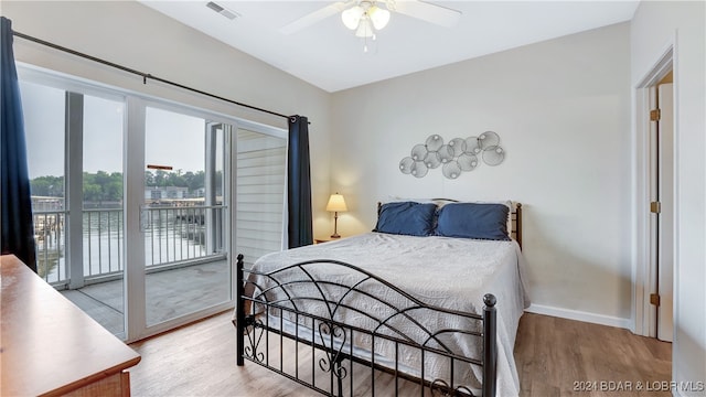 bedroom featuring access to outside, hardwood / wood-style flooring, a water view, and ceiling fan