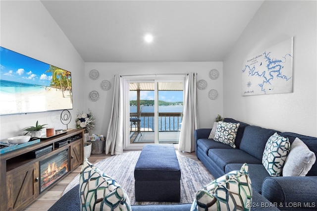 living room with light wood-type flooring, a water view, and lofted ceiling