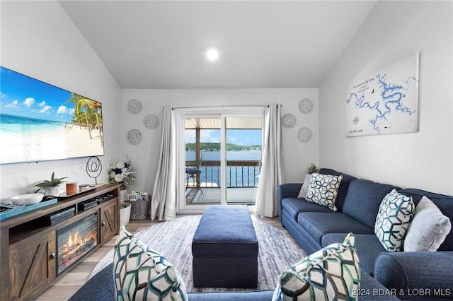 living area with light wood-type flooring, a water view, and vaulted ceiling