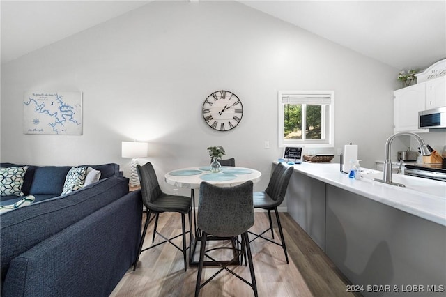 dining area with high vaulted ceiling and light wood-style flooring