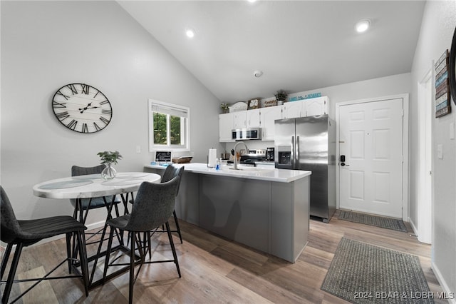 kitchen with white cabinets, a kitchen bar, appliances with stainless steel finishes, and light hardwood / wood-style flooring