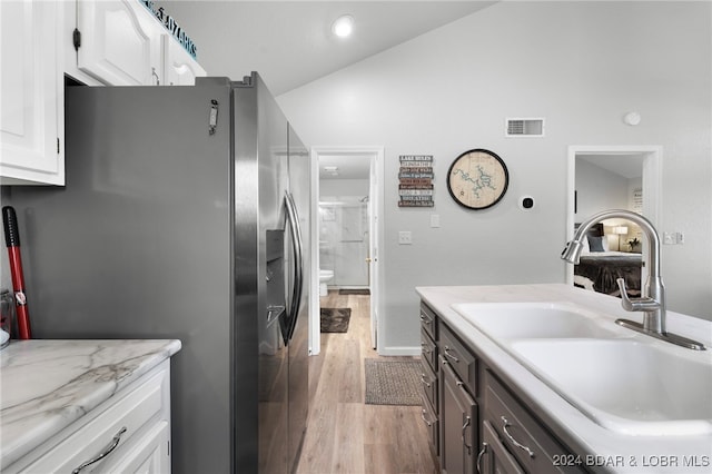 kitchen featuring sink, stainless steel refrigerator with ice dispenser, lofted ceiling, white cabinets, and light wood-type flooring