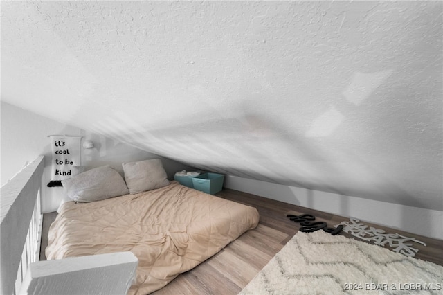 bedroom featuring a textured ceiling, hardwood / wood-style floors, and vaulted ceiling