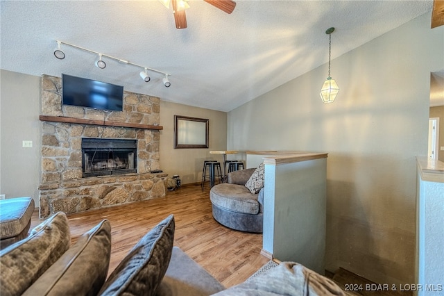 living room with lofted ceiling, hardwood / wood-style floors, ceiling fan, a textured ceiling, and a stone fireplace