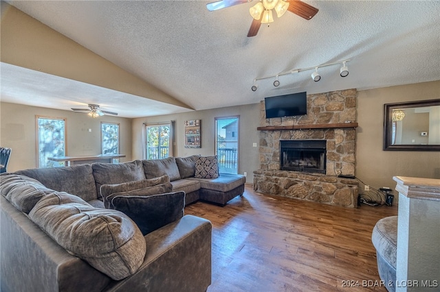 living room featuring lofted ceiling, a stone fireplace, hardwood / wood-style floors, a textured ceiling, and ceiling fan