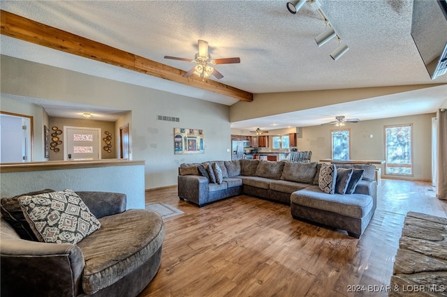 living room featuring lofted ceiling with beams, wood-type flooring, and a textured ceiling