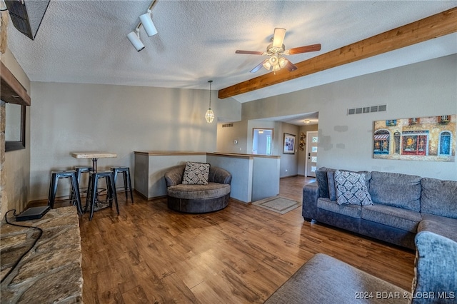 living room with a textured ceiling, hardwood / wood-style flooring, beamed ceiling, and ceiling fan