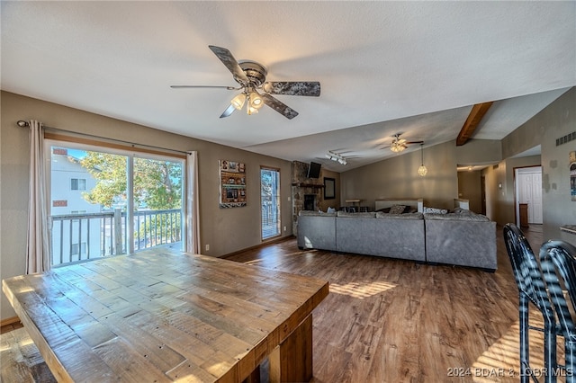 unfurnished living room featuring a stone fireplace, vaulted ceiling with beams, dark hardwood / wood-style floors, and ceiling fan