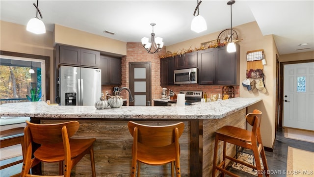 kitchen with kitchen peninsula, dark brown cabinets, a breakfast bar area, stainless steel appliances, and decorative light fixtures