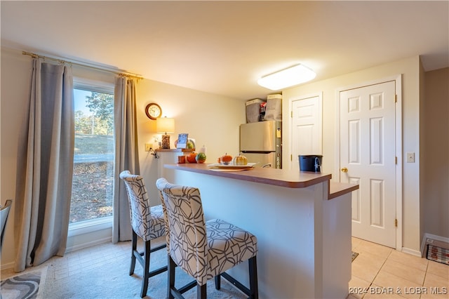 kitchen with light tile patterned flooring, a breakfast bar area, kitchen peninsula, and stainless steel fridge