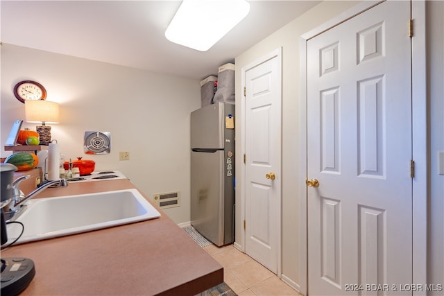 kitchen featuring sink, light tile patterned floors, and stainless steel refrigerator