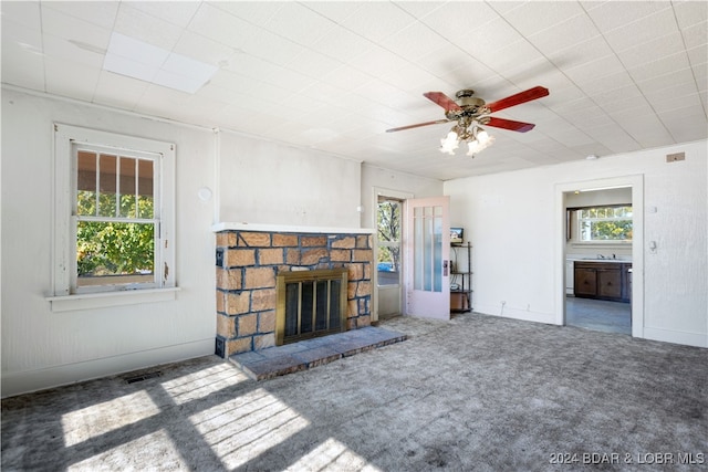 unfurnished living room with a stone fireplace, carpet floors, sink, and ceiling fan