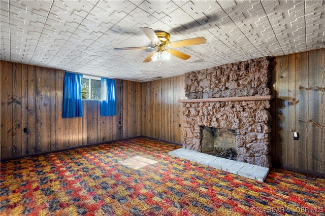 unfurnished living room featuring a stone fireplace, wooden walls, and dark colored carpet