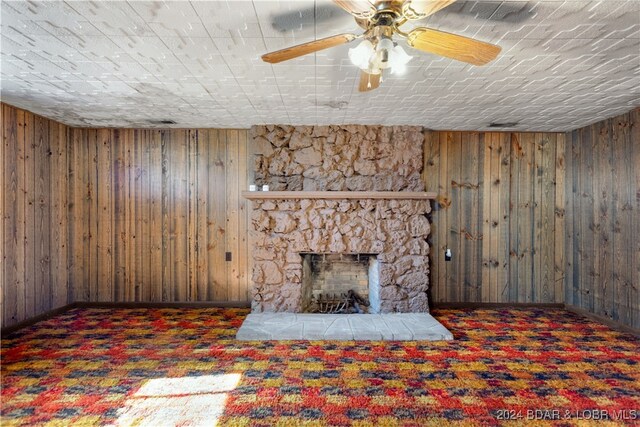 unfurnished living room featuring dark carpet, a stone fireplace, and wood walls