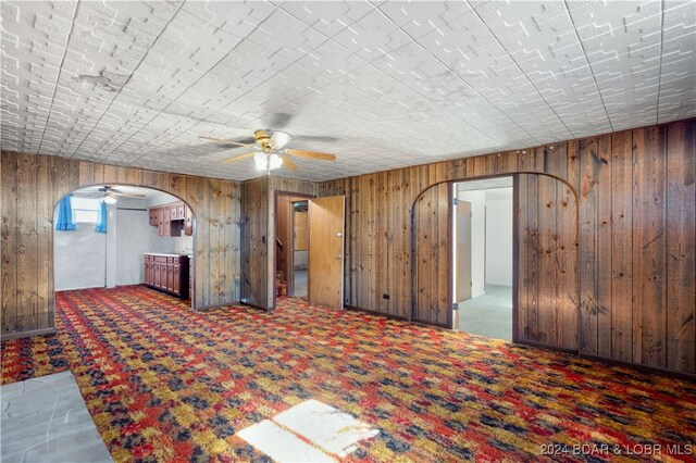 interior space featuring wooden walls, dark carpet, and ceiling fan