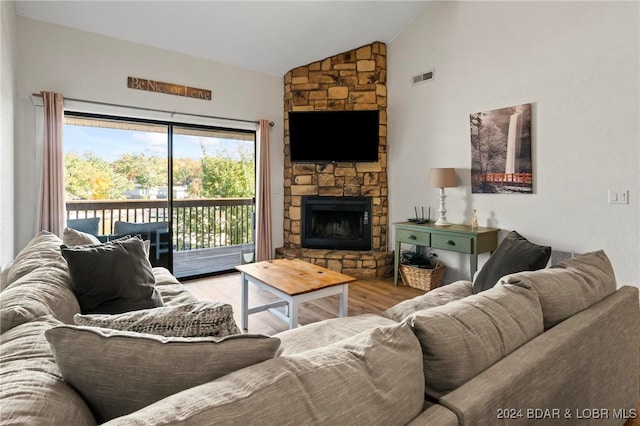 living room featuring vaulted ceiling, a stone fireplace, and light wood-type flooring