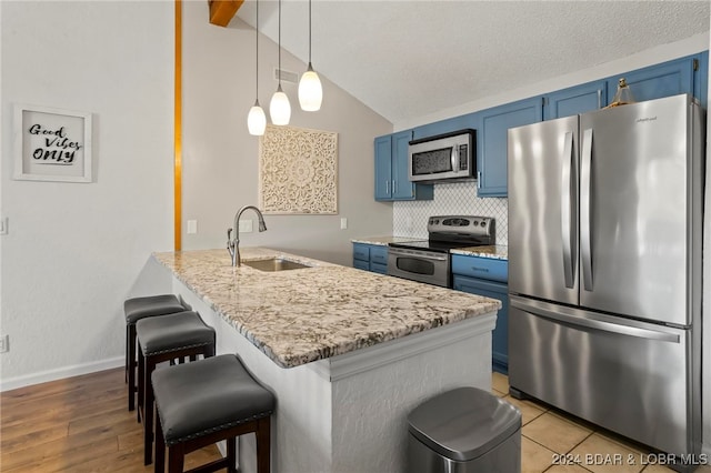 kitchen featuring hanging light fixtures, vaulted ceiling, blue cabinetry, sink, and stainless steel appliances