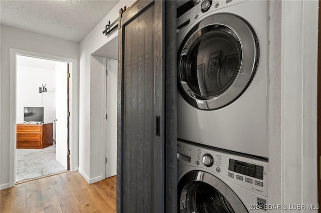 laundry area featuring a barn door, stacked washer and clothes dryer, a textured ceiling, and light wood-type flooring