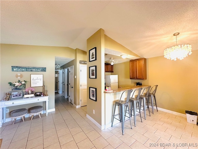 kitchen with kitchen peninsula, hanging light fixtures, a chandelier, vaulted ceiling, and white refrigerator