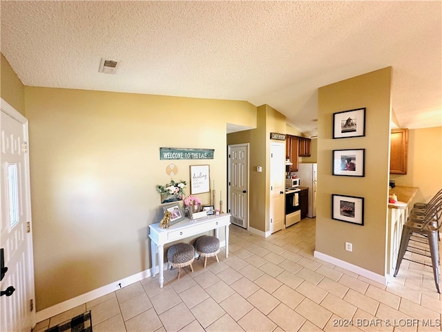 hallway with light tile patterned floors, a textured ceiling, and vaulted ceiling