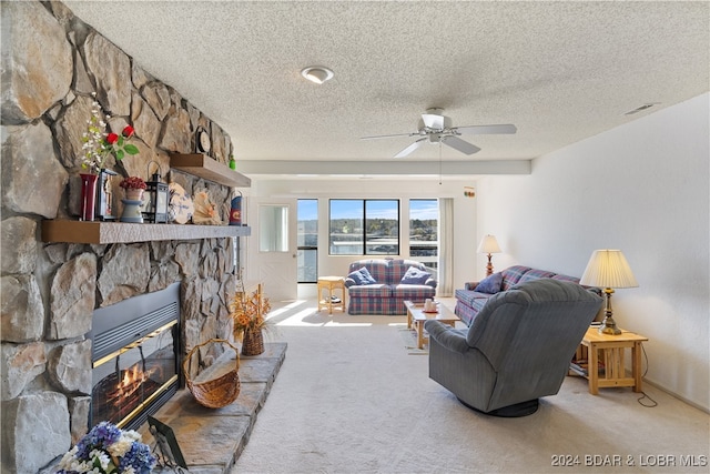 carpeted living room featuring ceiling fan, a stone fireplace, and a textured ceiling