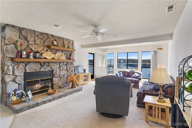 carpeted living room featuring a textured ceiling, a stone fireplace, and ceiling fan