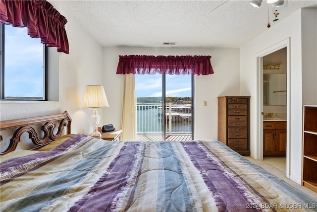 bedroom featuring a water view, ceiling fan, access to exterior, a textured ceiling, and connected bathroom