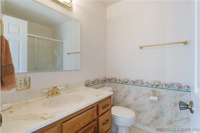 bathroom with vanity, a shower with door, tile patterned floors, toilet, and tile walls