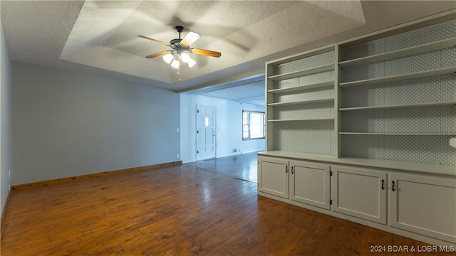 interior space with a textured ceiling, ceiling fan, a tray ceiling, and dark hardwood / wood-style flooring