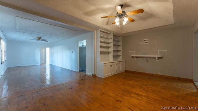 empty room with ceiling fan, hardwood / wood-style flooring, a textured ceiling, and a tray ceiling