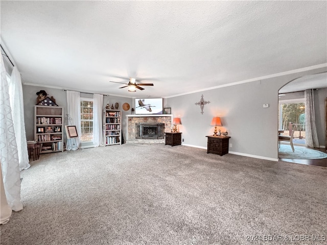 unfurnished living room featuring a stone fireplace, ornamental molding, carpet, a textured ceiling, and ceiling fan