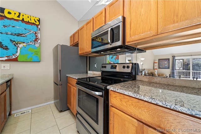 kitchen with appliances with stainless steel finishes, lofted ceiling, light stone counters, and light tile patterned floors