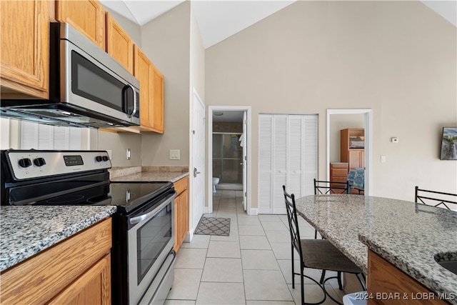 kitchen featuring light stone counters, stainless steel appliances, high vaulted ceiling, and light tile patterned floors