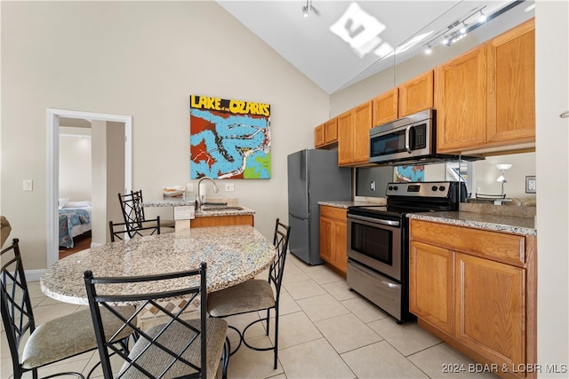 kitchen with appliances with stainless steel finishes, sink, track lighting, vaulted ceiling, and light tile patterned floors