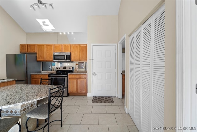 kitchen featuring appliances with stainless steel finishes, light stone counters, vaulted ceiling, and light tile patterned floors