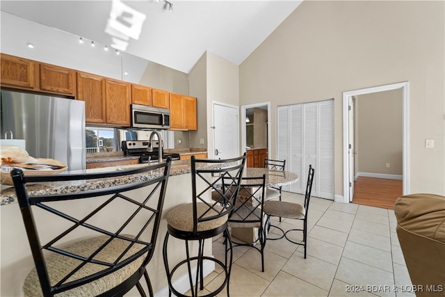 kitchen with a breakfast bar area, appliances with stainless steel finishes, rail lighting, light tile patterned floors, and high vaulted ceiling