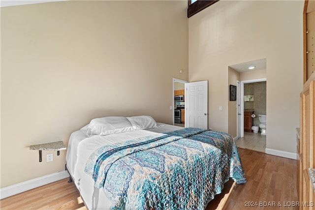 bedroom with hardwood / wood-style floors, ensuite bathroom, and a high ceiling