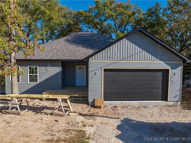 ranch-style home featuring an attached garage, a shingled roof, and board and batten siding