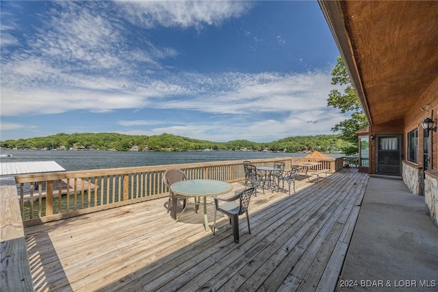 wooden terrace featuring a water view, a view of trees, and outdoor dining space