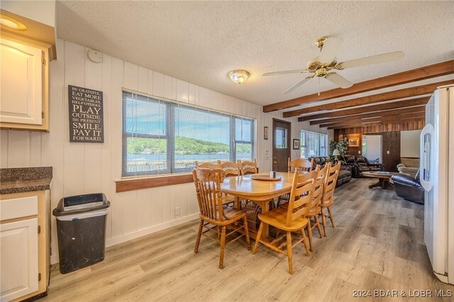 dining space with a textured ceiling, ceiling fan, beam ceiling, light hardwood / wood-style flooring, and wood walls